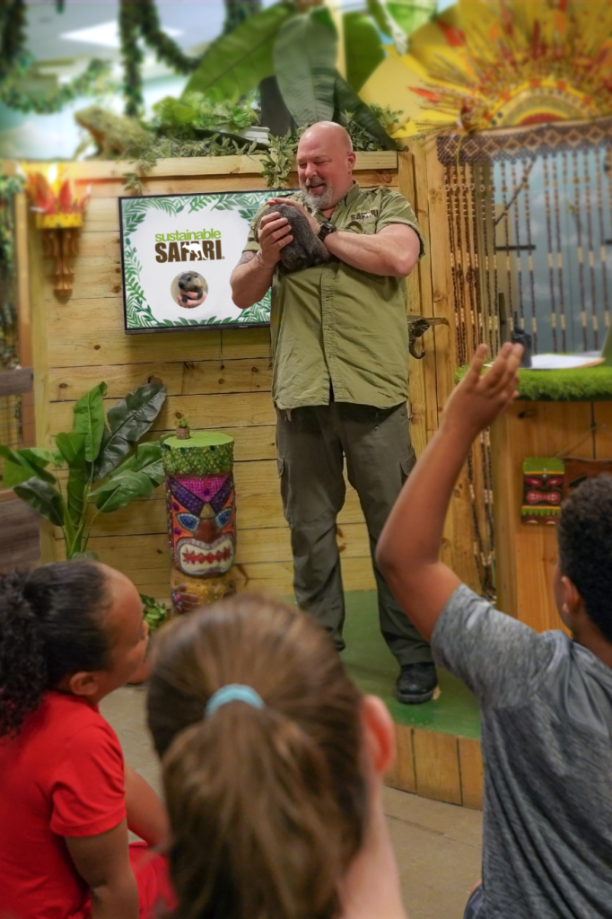Wildlife show, a man holding a groundhog on stage showing a small crowd, a young boy holds his hand up to ask a question