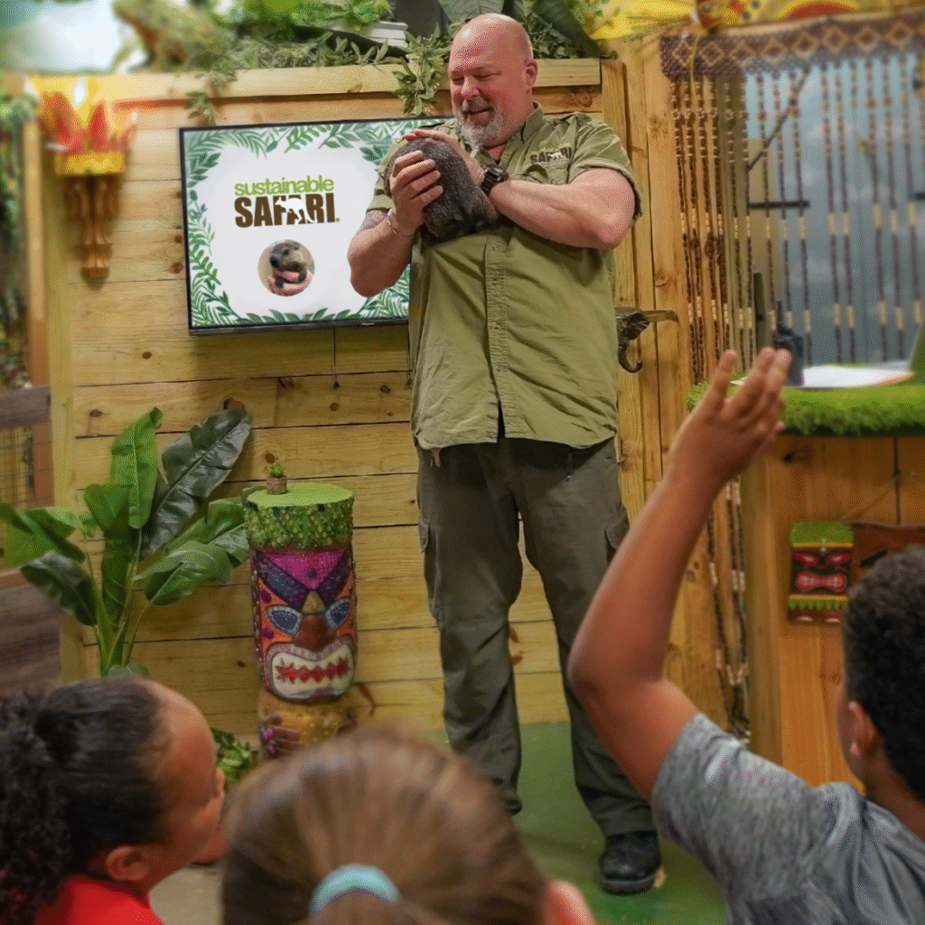 Wildlife show, a man holding a groundhog on stage showing a small crowd, a young boy holds his hand up to ask a question