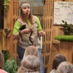 wildlife show children watching a woman speak with a large snake in her hands