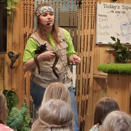 wildlife show children watching a woman speak with a large snake in her hands