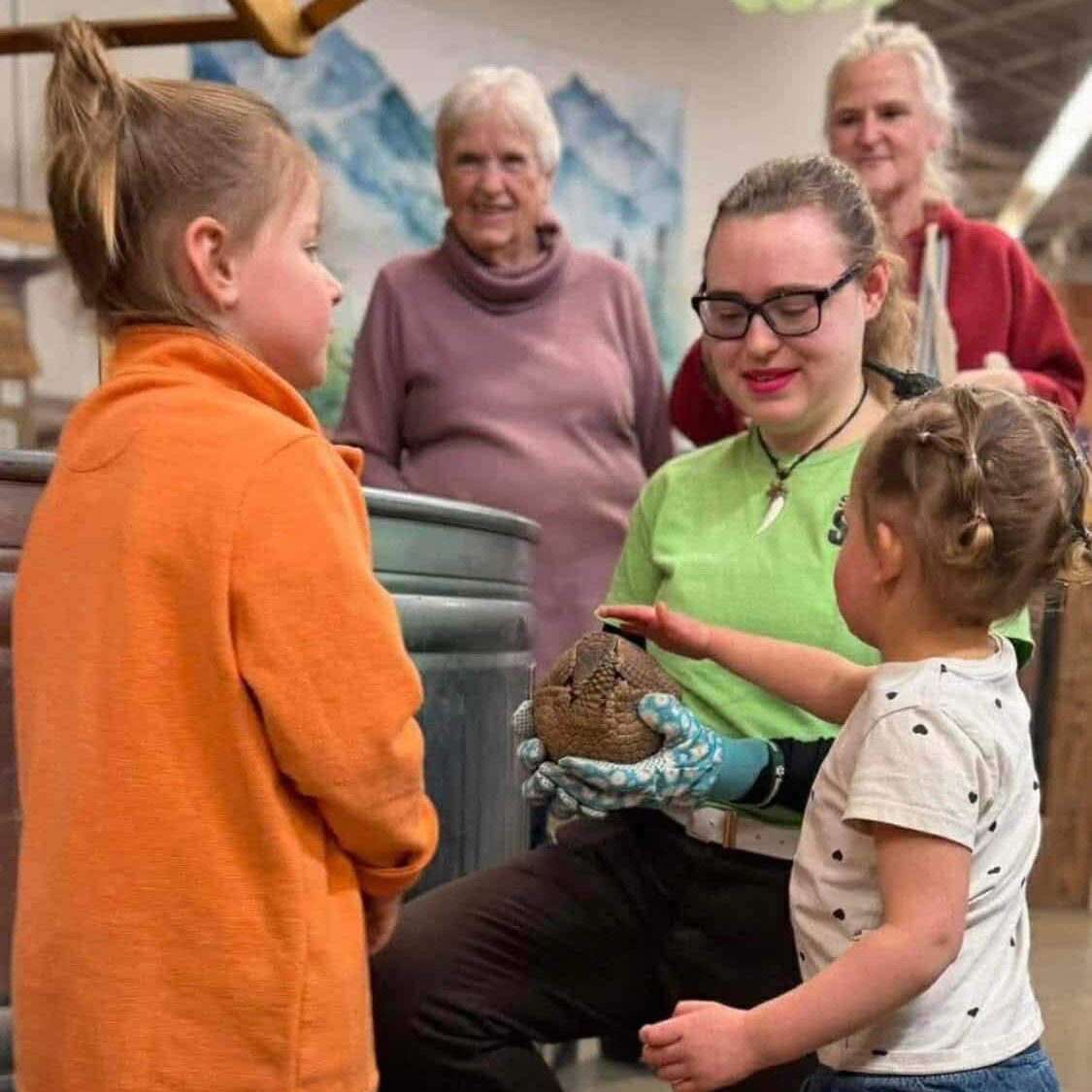 young children petting an armadillo that an employee is holding